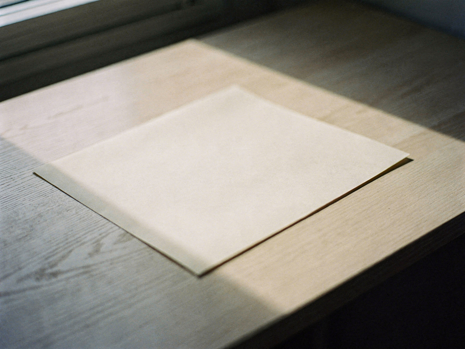 A single sheet of warm cream paper resting on a pale oak desk in soft afternoon window light